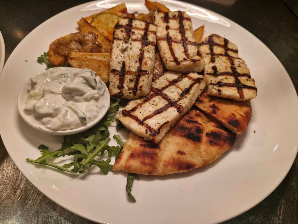 Gegrillter Halloumi, Pitabrot, Kartoffeln und Tzatziki-Sauce auf einem weissen Teller.