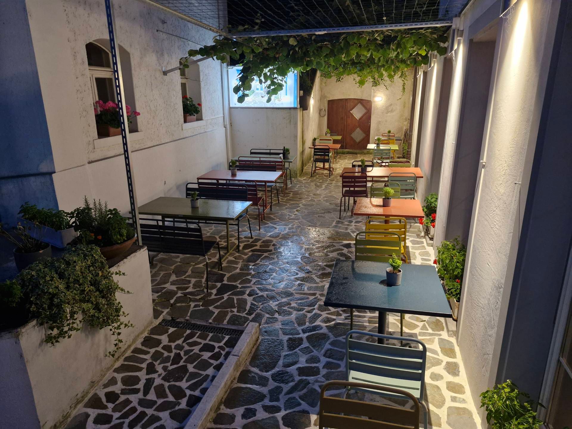 Restauranthof im Freien mit Tischen und Stühlen unter einer weinbewachsenen Pergola und gedämpfter Beleuchtung.