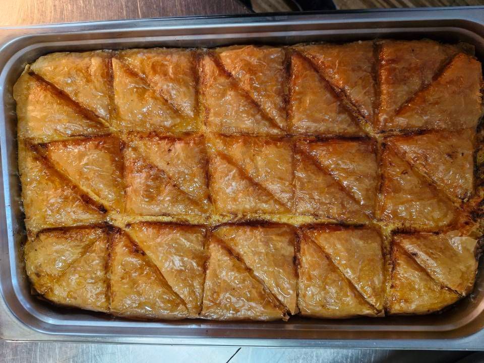 Baklava, ein goldbraunes Gebäck, das in Dreiecke geschnitten und auf einem rechteckigen Metalltablett präsentiert wird.