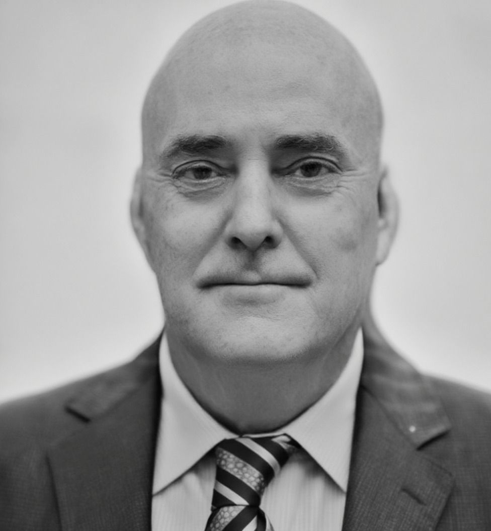Una fotografía en blanco y negro de un hombre que lleva una chaqueta oscura