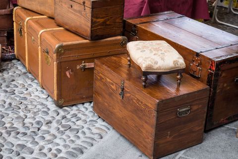 Des malles en bois anciennes empilées sur une rue pavée, avec un petit tabouret dessus.