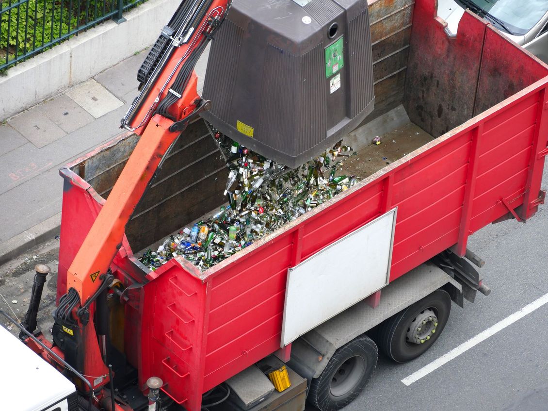 Un camion-benne rouge est chargé de verre concassé par le bras d'une grue dans une rue.