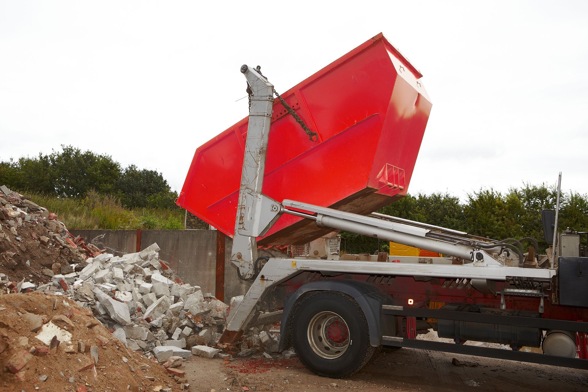 Camion-benne rouge déversant des gravats sur un site de déchets de construction.