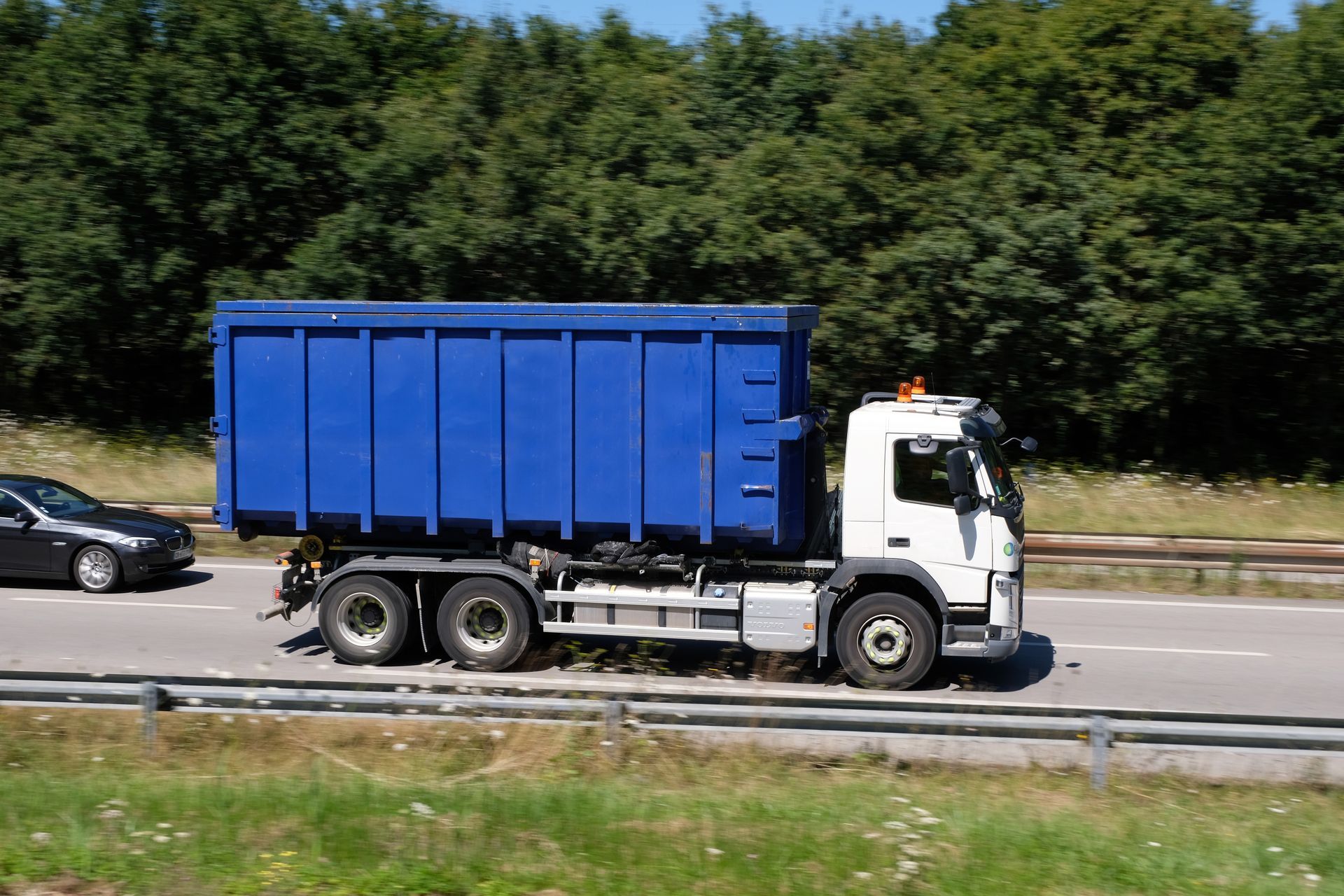Un camion-benne bleu circule sur une autoroute avec des arbres en arrière-plan.