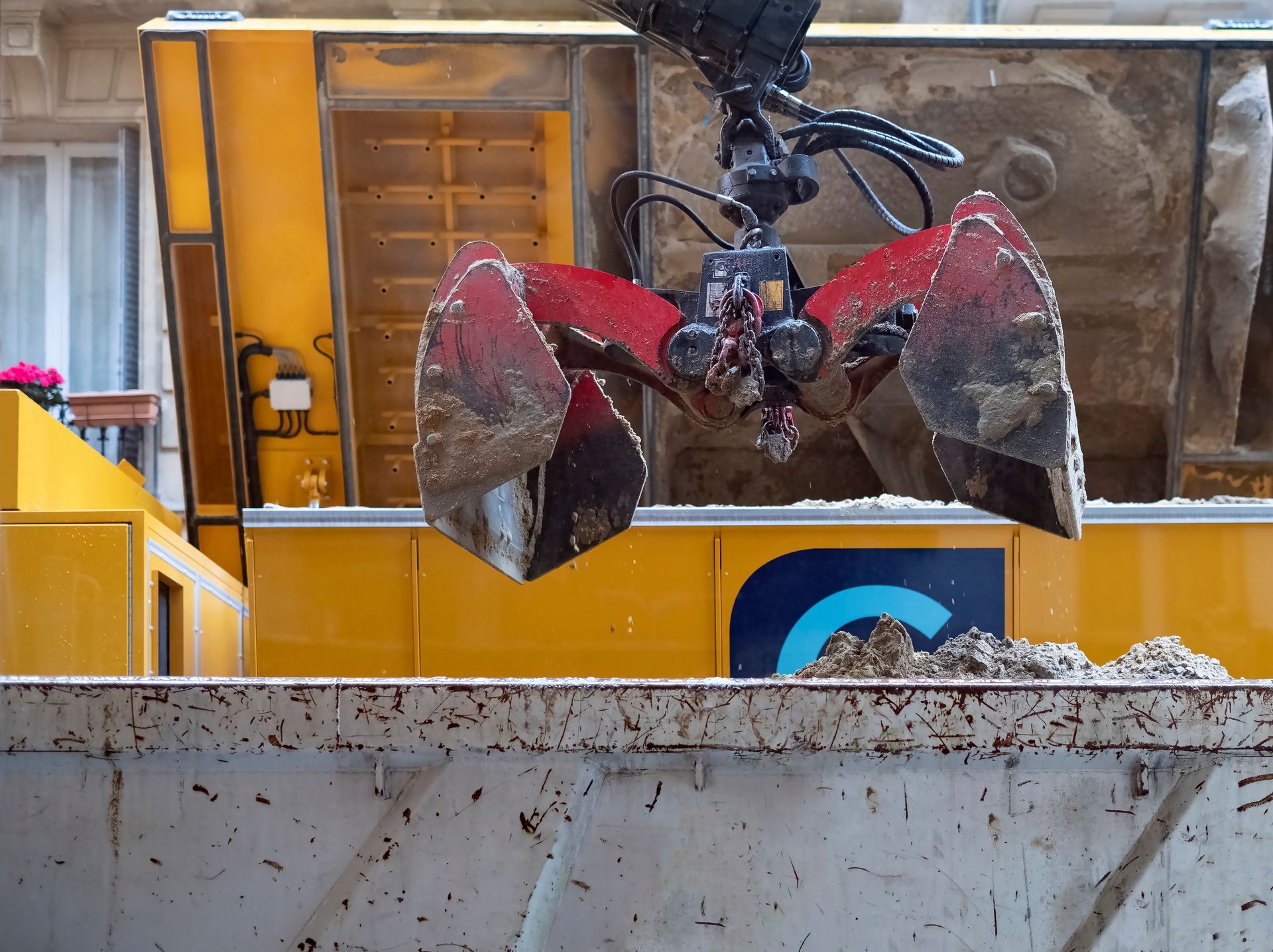 Une pelle mécanique à griffes rouges franchit une barrière en béton sur un chantier de construction.