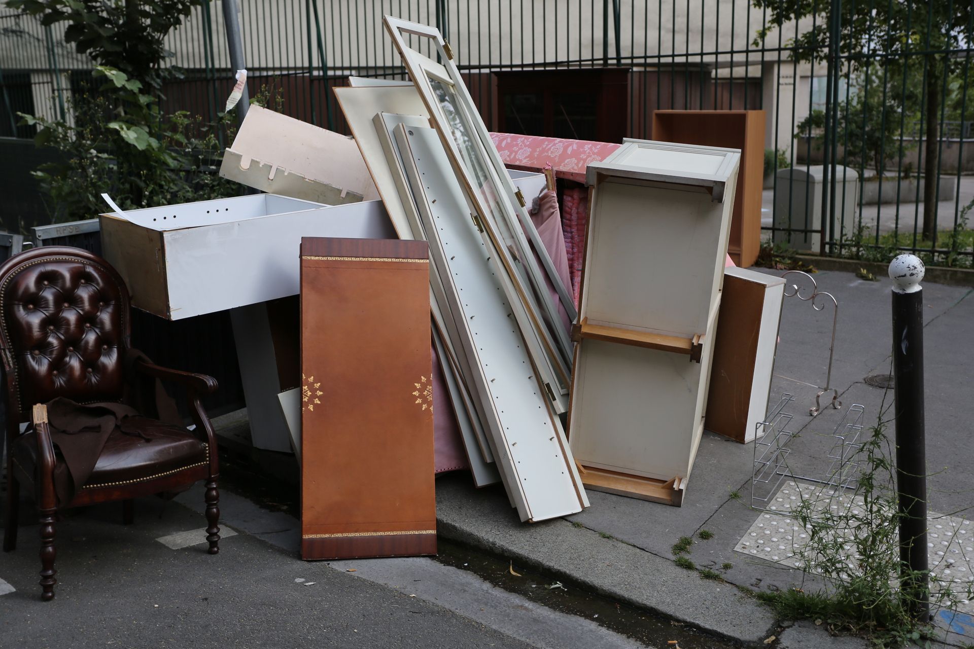 Des meubles et des étagères abandonnés, entassés sur un trottoir à côté d'un immeuble.