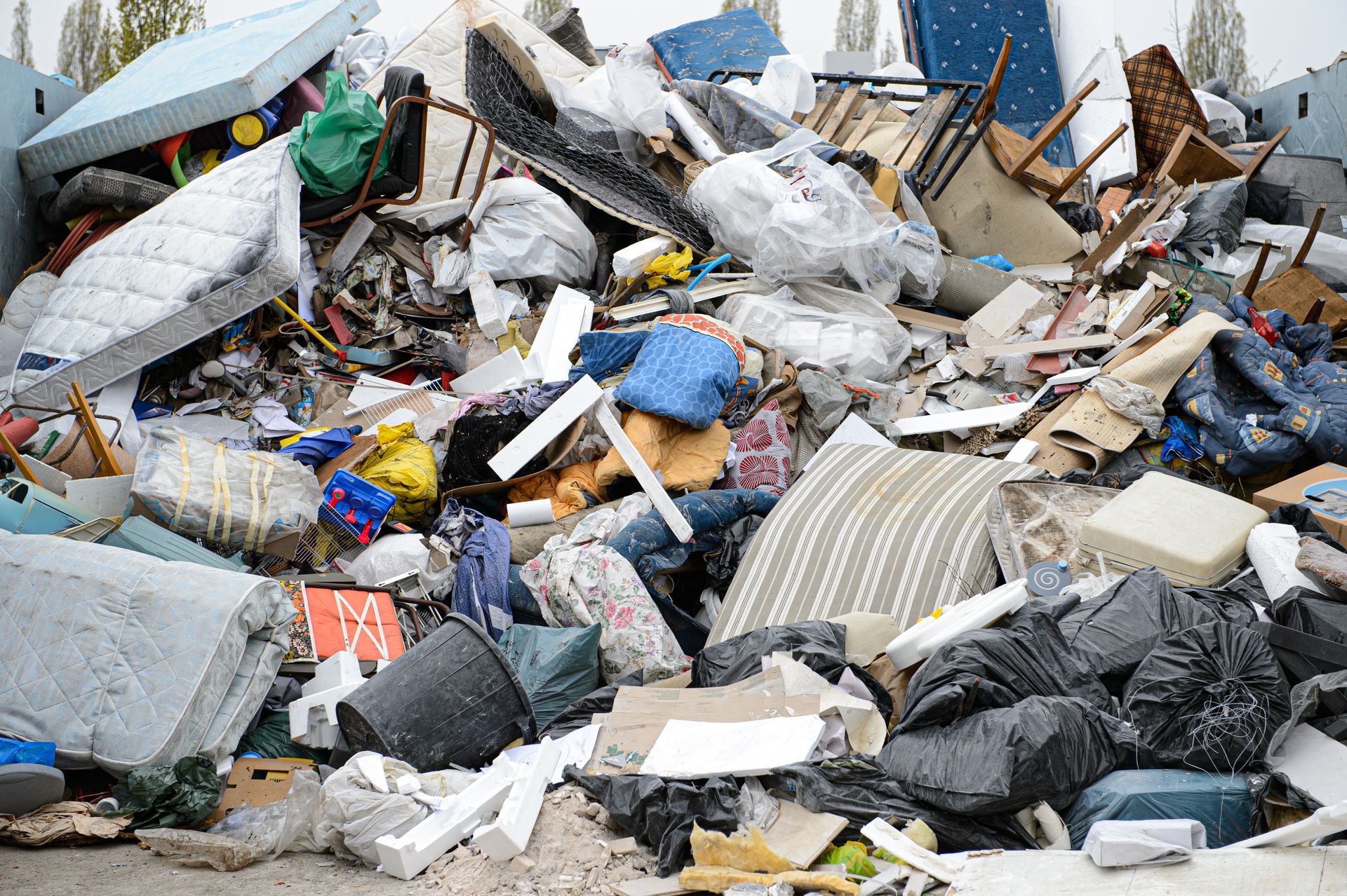 Tas de déchets et de débris mélangés, comprenant des sacs, du carton et des meubles cassés, sur un site de décharge à ciel ouvert