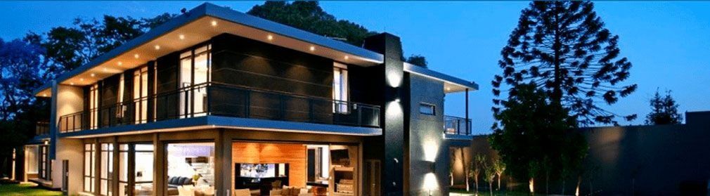 Casa moderna de dos pisos al capvespre. Grans finestres revelen una càlida il·luminació interior. Focus exteriors il·luminen la façana.