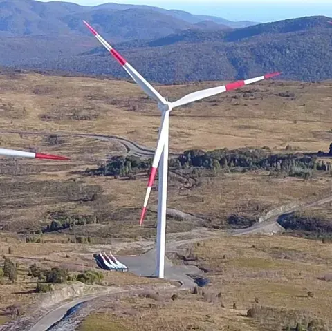 Una vista aérea de una turbina eólica en un campo con montañas al fondo.