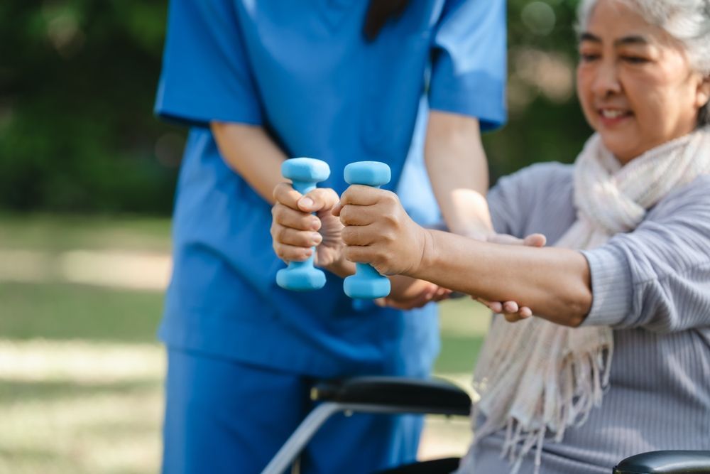Una enfermera está ayudando a una anciana en silla de ruedas a levantar pesas.