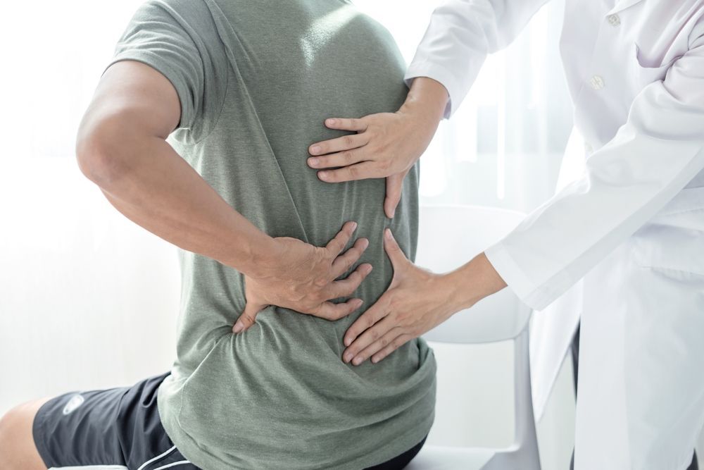 Un hombre está arrodillado mientras un médico le examina la espalda.
