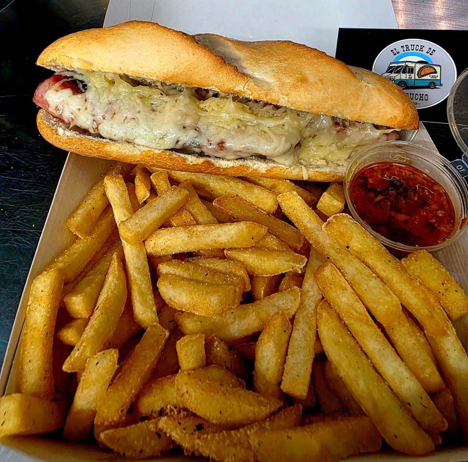 Ein langes Sandwich mit geschmolzenem Käse, serviert mit goldgelben Pommes frites und einem kleinen Schälchen roter Sosse.