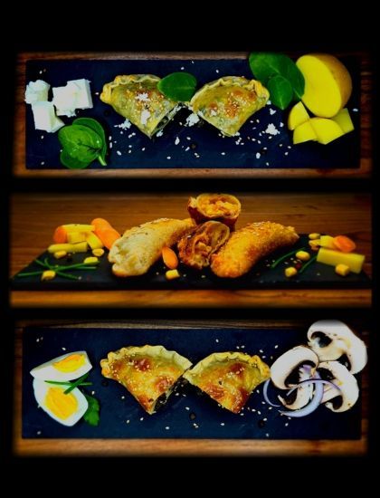 Auf drei Schieferplatten werden verschiedene gefüllte, herzhafte Gebäckstücke präsentiert, die mit frischen Garnierungen wie Käse, Eiern und Kräutern serviert werden.