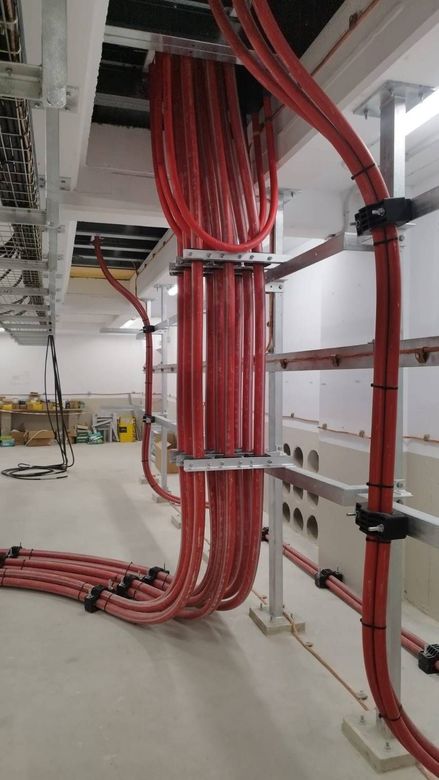 Dos trabajadores de servicios públicos con chalecos y cascos de color naranja trabajan en líneas eléctricas contra un cielo azul.