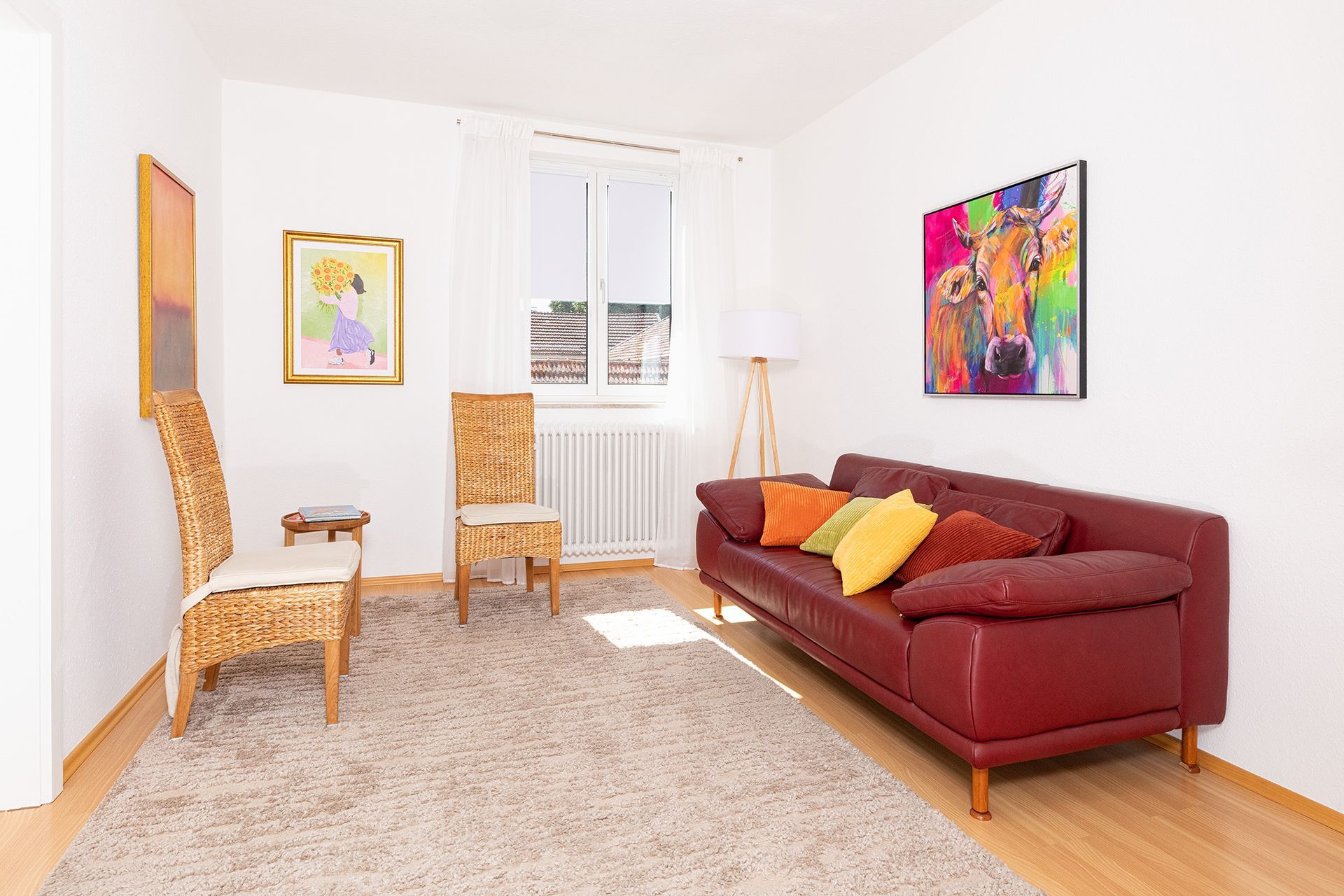 Heller Beratungsraum mit Sofa, Sesseln, Holzmöbeln und farbenfrohen Bildern an den Wänden.