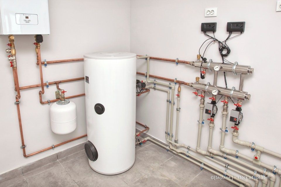 Komponenten der Heizungsanlage, darunter ein Warmwasserbereiter, ein Heizkessel und Kupferrohre, die in einem Hauswirtschaftsraum installiert sind.
