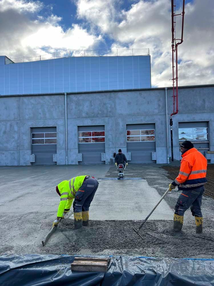 Eine Gruppe Bauarbeiter arbeitet an einer Betoneinfahrt vor einem Gebäude.