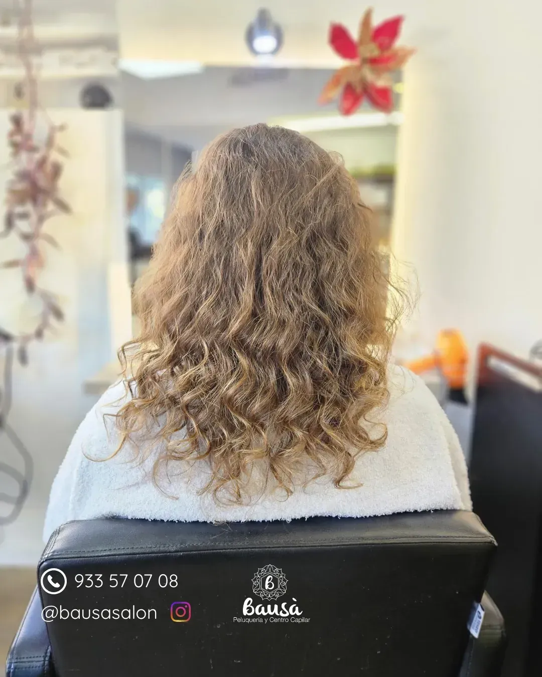 Una persona con cabello largo, rizado y castaño claro está sentada en una silla de peluquería, de espaldas a la cámara.