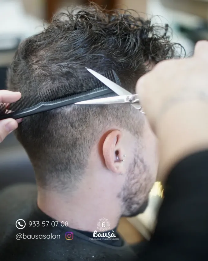 Un estilista utiliza tijeras y un peine para recortar el cabello de la parte posterior y los lados de la cabeza del cliente.