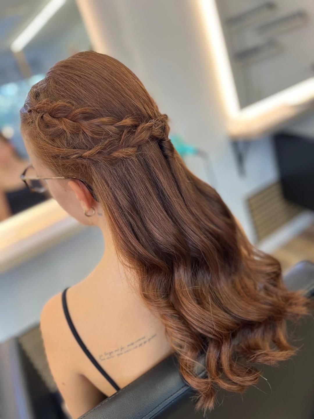 Una persona con cabello largo, ondulado y castaño rojizo, peinado en un semirecogido con una corona trenzada decorativa.