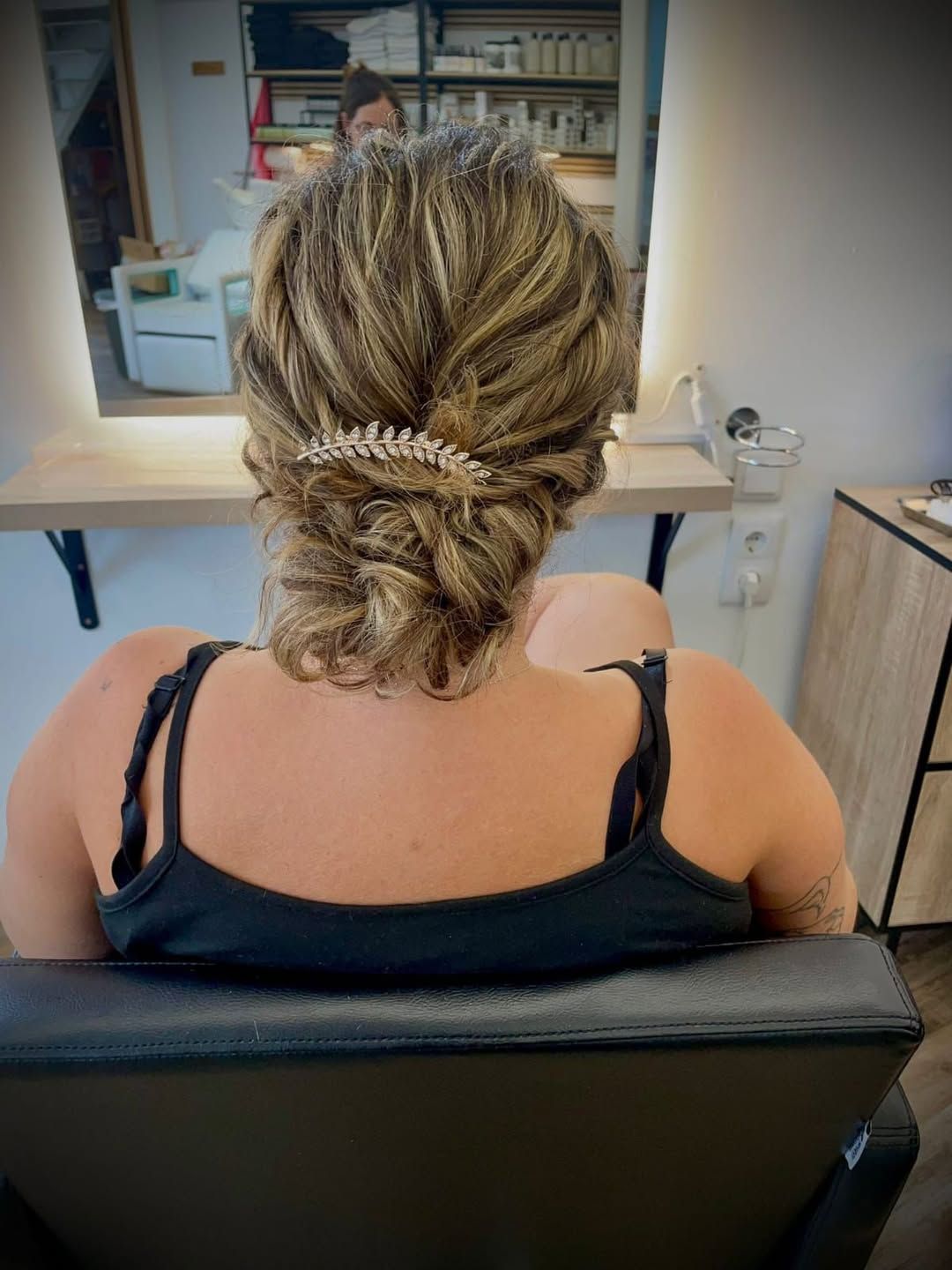 Una persona sentada en una silla de peluquería con el cabello con mechas recogido en un moño bajo texturizado, adornado .