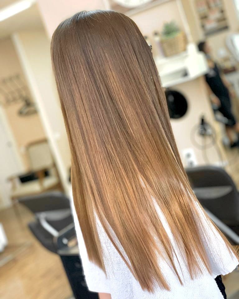 Una persona con cabello largo, liso y castaño claro, vista de espaldas en una peluquería.