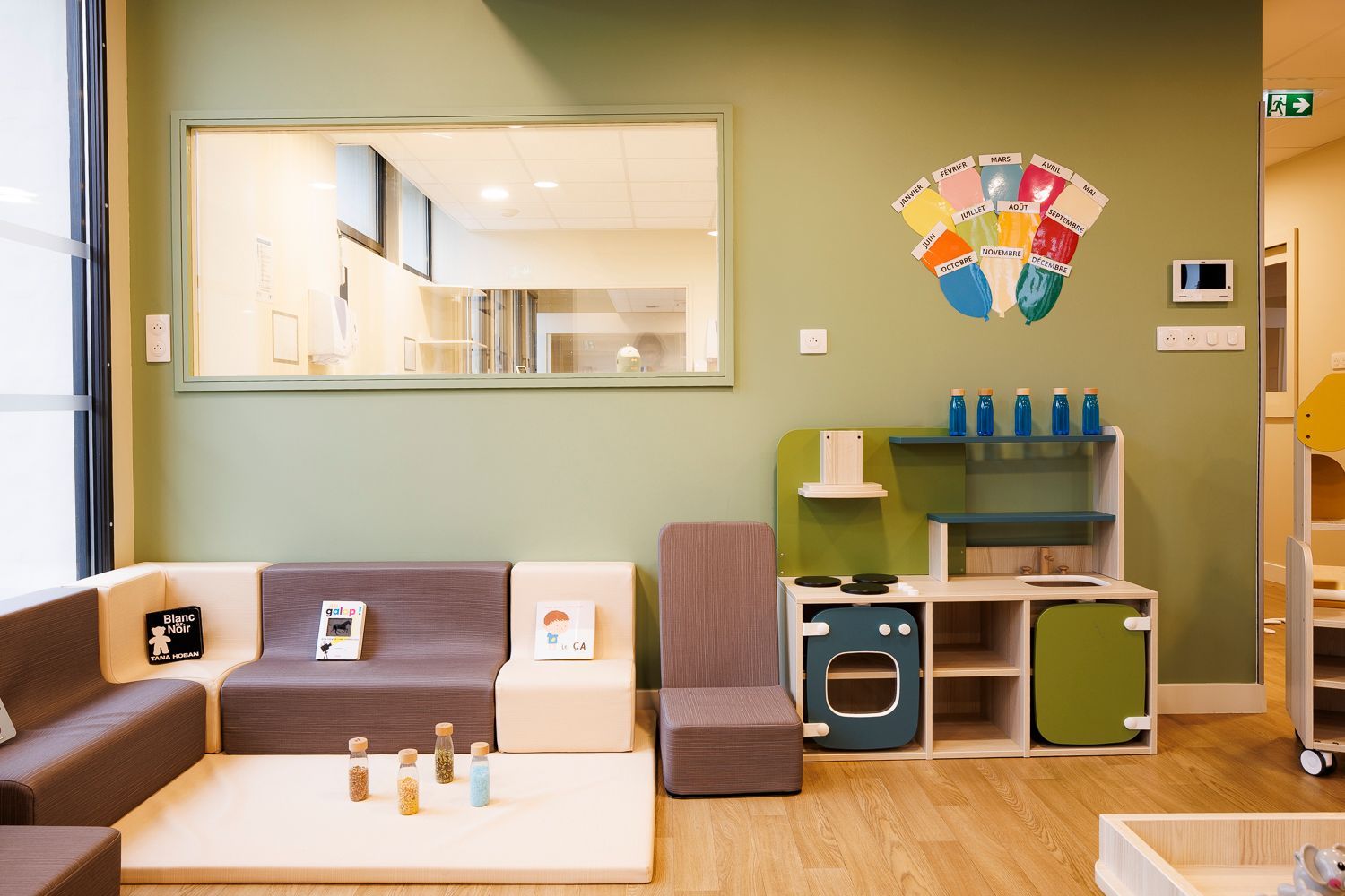 Présentation d'une pièce avec une cuisine pour enfant et des petits fauteuils de couleurs pour s'assoir.