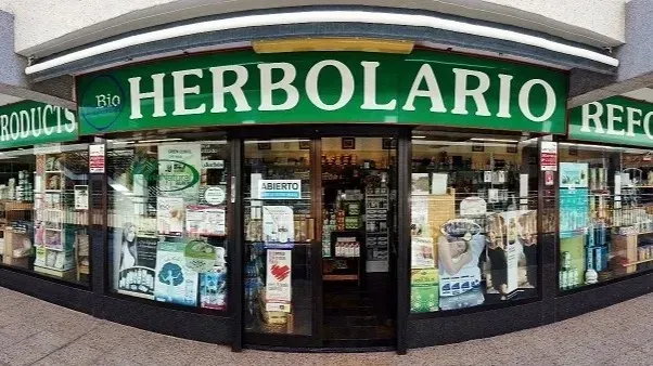 La fachada de una tienda de alimentos naturales llamada Herbolario, con un letrero verde y escaparates.