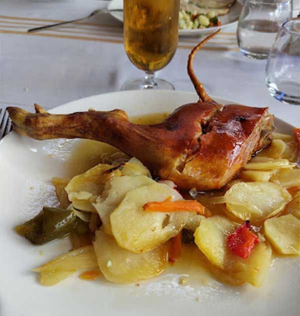 Un plato blanco cubierto con carne y patatas con un vaso de cerveza de fondo.