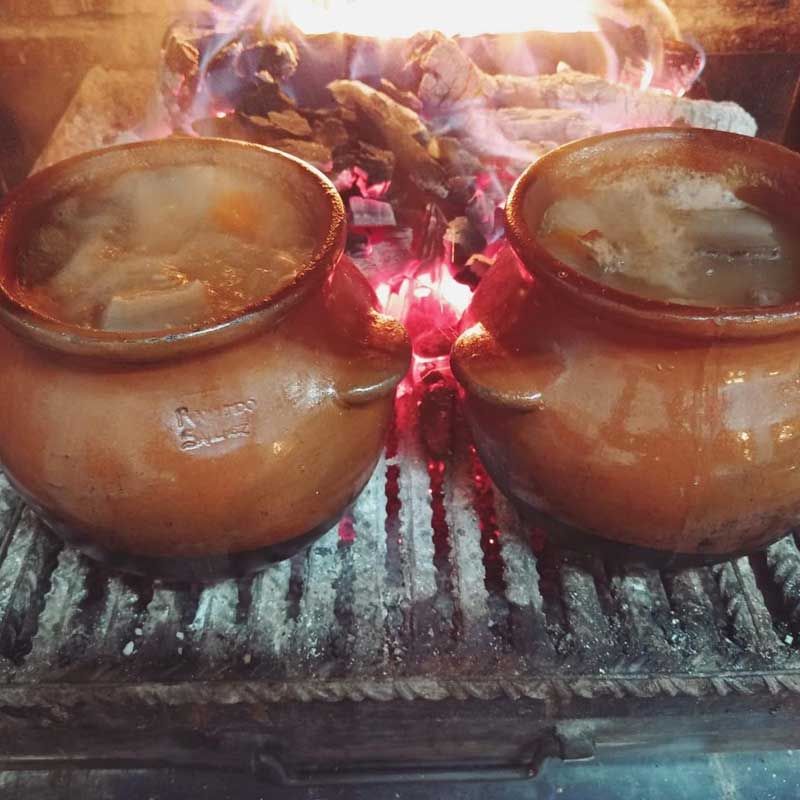 Dos ollas de barro llenas de comida están colocadas sobre una parrilla sobre el fuego.