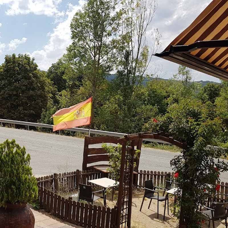 Una bandera española ondea sobre un patio con mesas y sillas.