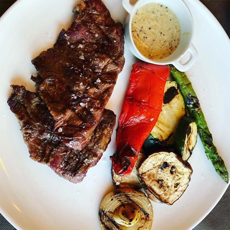 Un plato blanco cubierto con un filete y verduras.