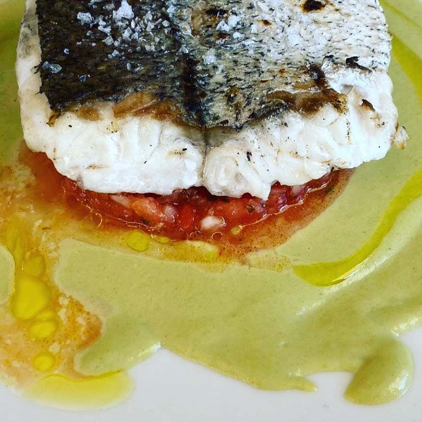 Un plato blanco cubierto con un trozo de pescado y tomates.
