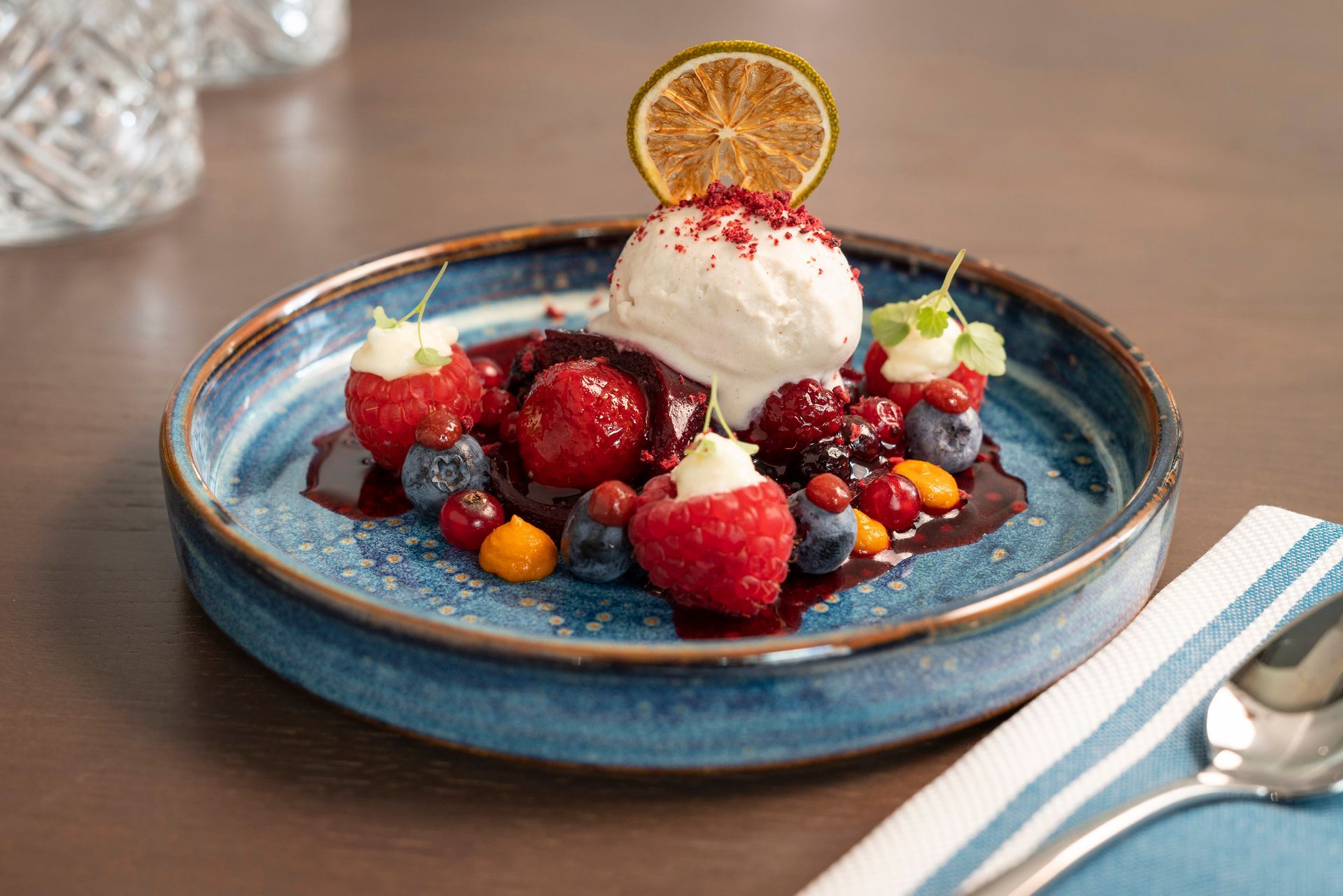 Ein Dessertteller mit einer Kugel Vanilleeis, garniert mit einer Limettenscheibe, umgeben von frischen Beeren und Sauce.