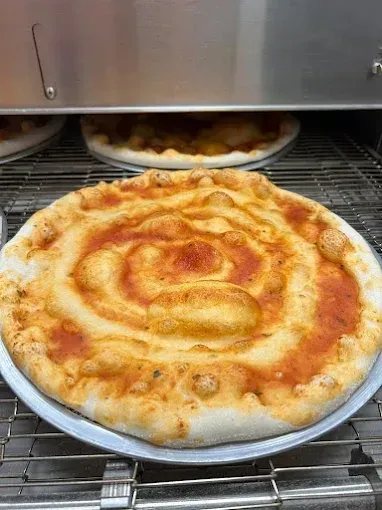 Una pizza con salsa de tomate en espiral horneándose sobre una rejilla metálica en un horno.