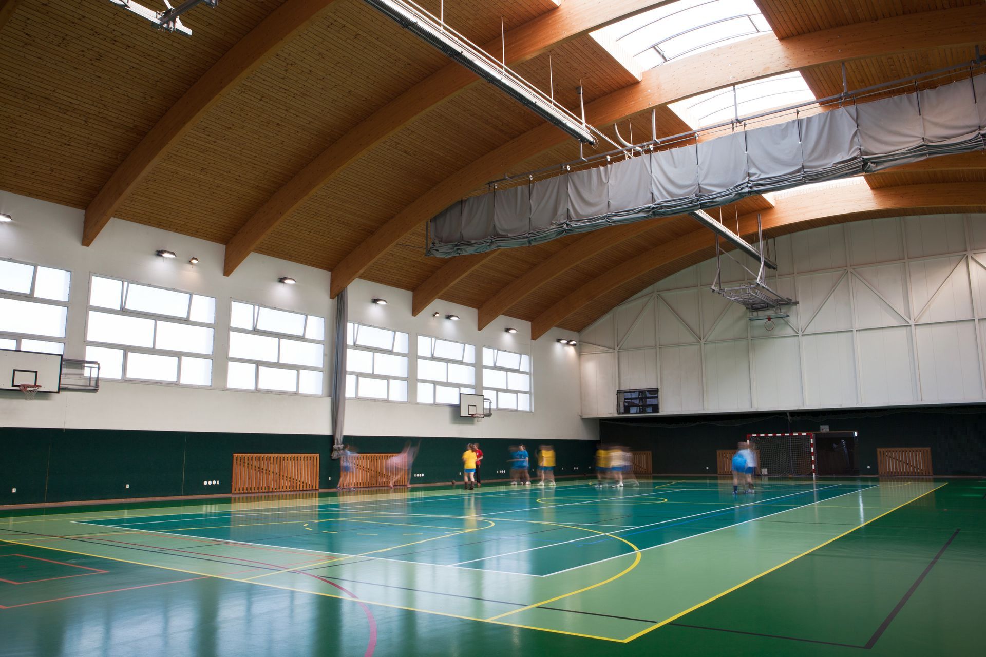 Une salle omnisports intérieure avec un terrain vert, un plafond voûté en bois et de hautes fenêtres le long du mur latéral.