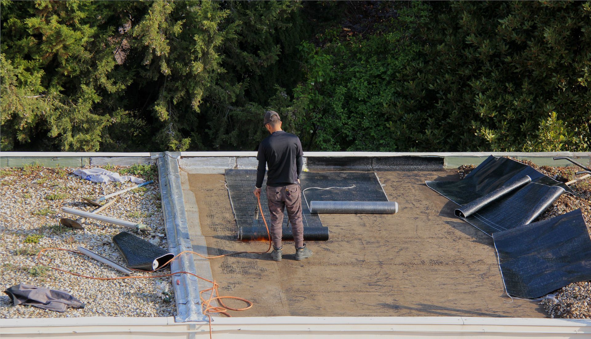 Une personne travaille sur un toit plat, en train d'installer des feuilles de membrane d'étanchéité.