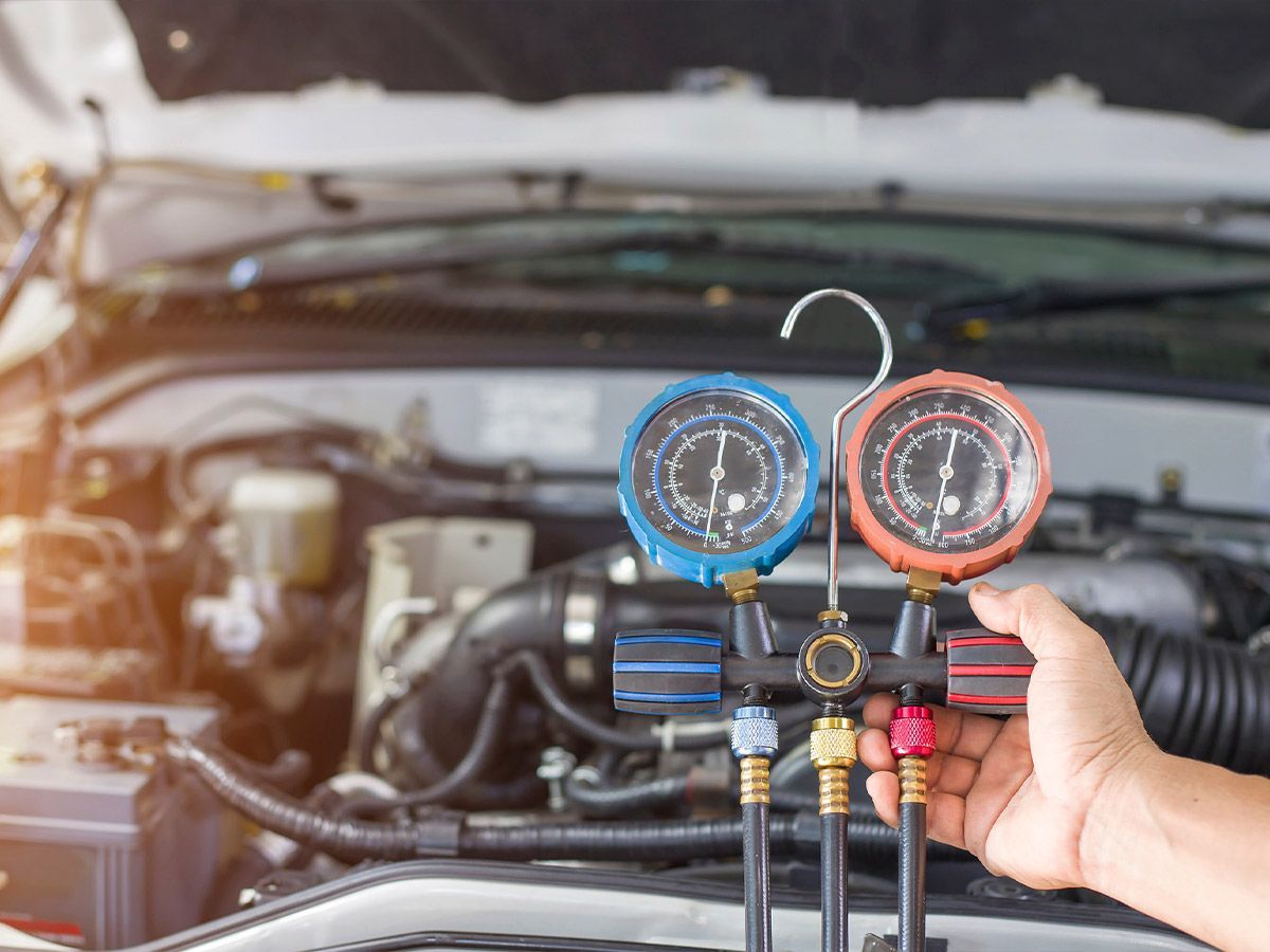 Una persona sostiene dos medidores delante del motor de un automóvil.