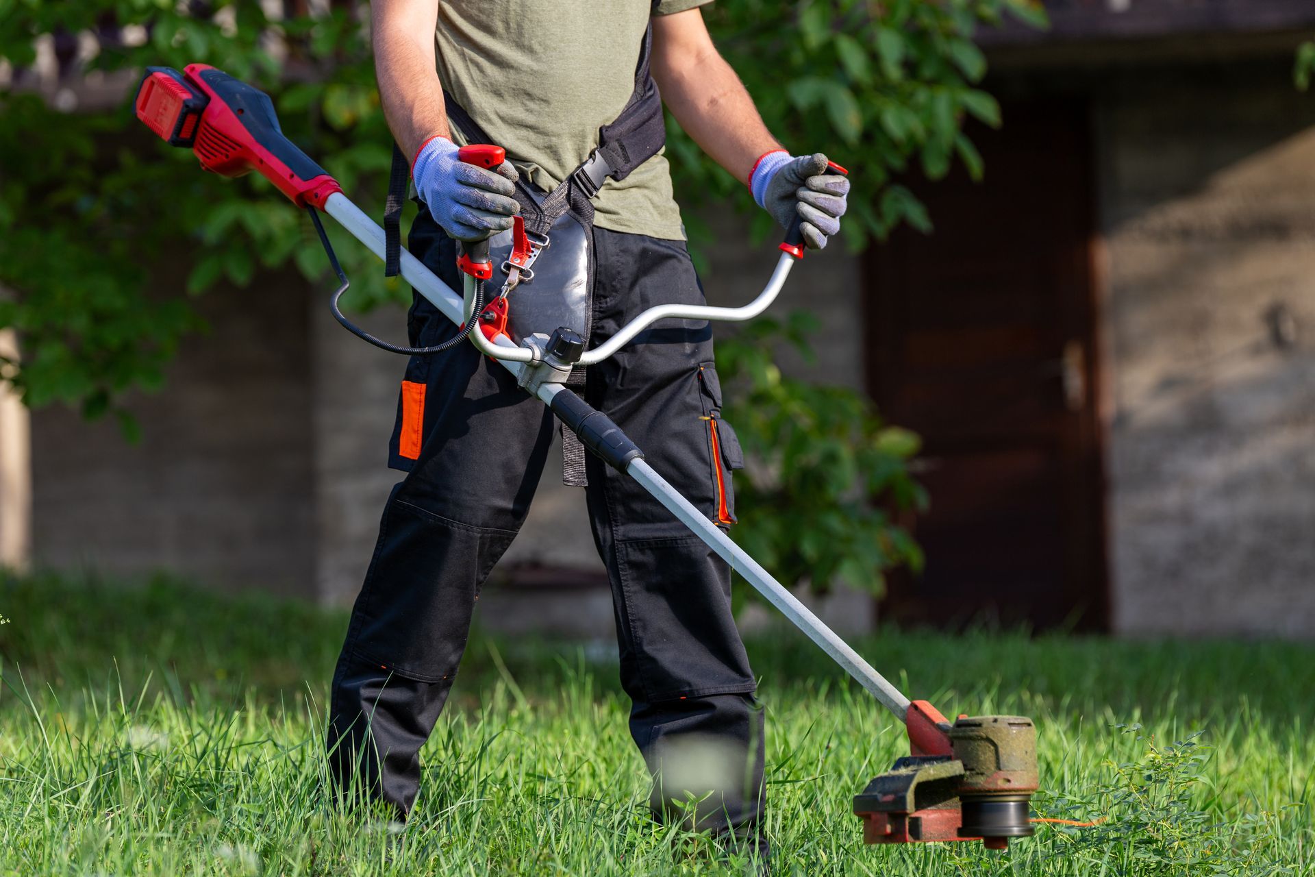 Person, die mit einem rot-schwarzen Rasentrimmer Gras schneidet.