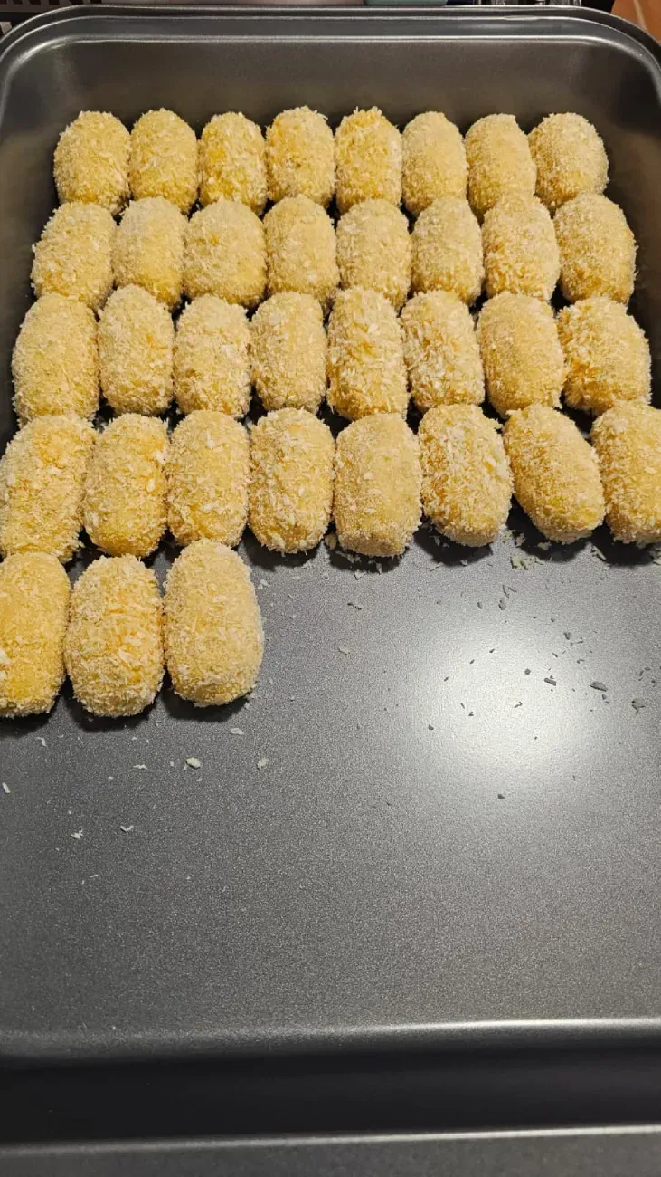 Bandeja de croquetas rebozadas y doradas, listas para cocinar, en bandeja de horno.