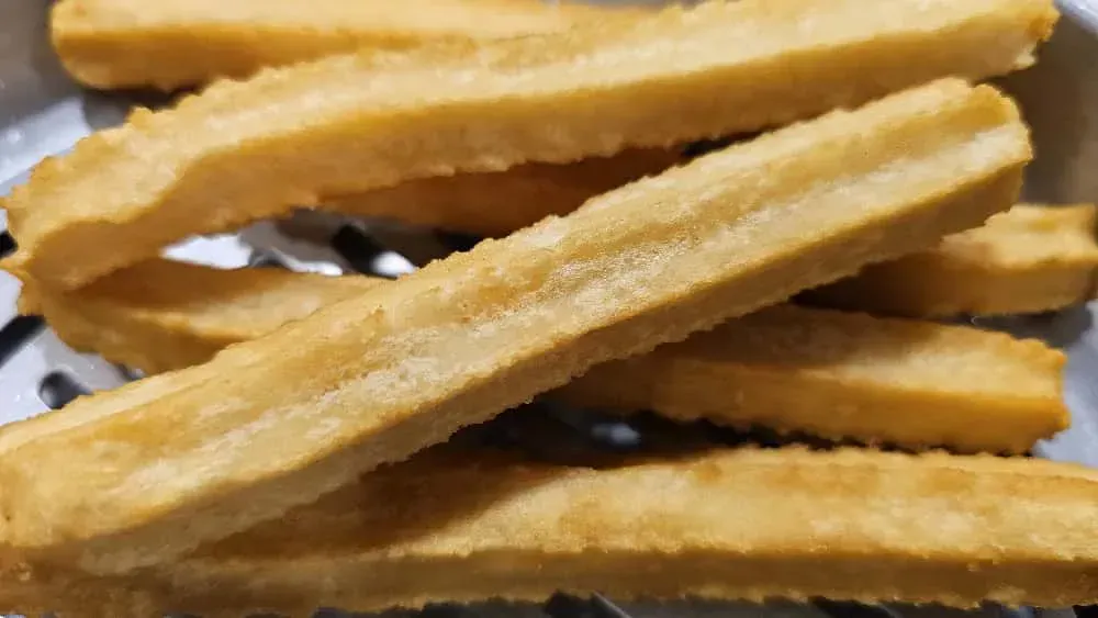 Primer plano de churros dorados apilados en un colador de metal, listos para comer.