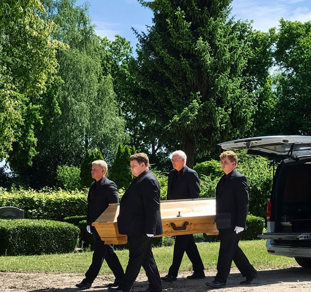 Ein Holzsarg wurde in den hinteren Teil eines Leichenwagens geladen, die Hecktür war offen.