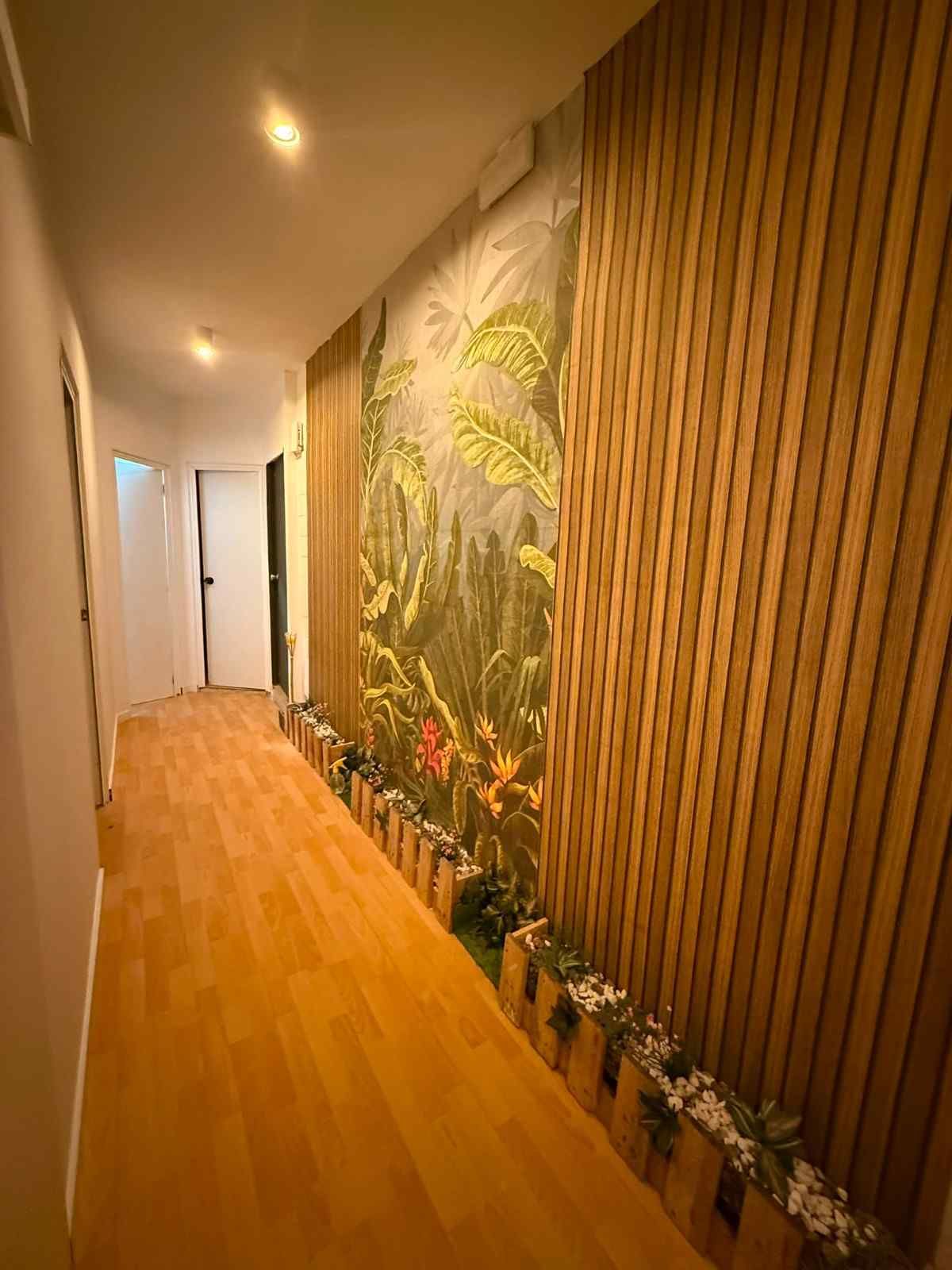 Pasillo estrecho con suelo de madera, mural tropical y revestimiento de madera vertical en las paredes.