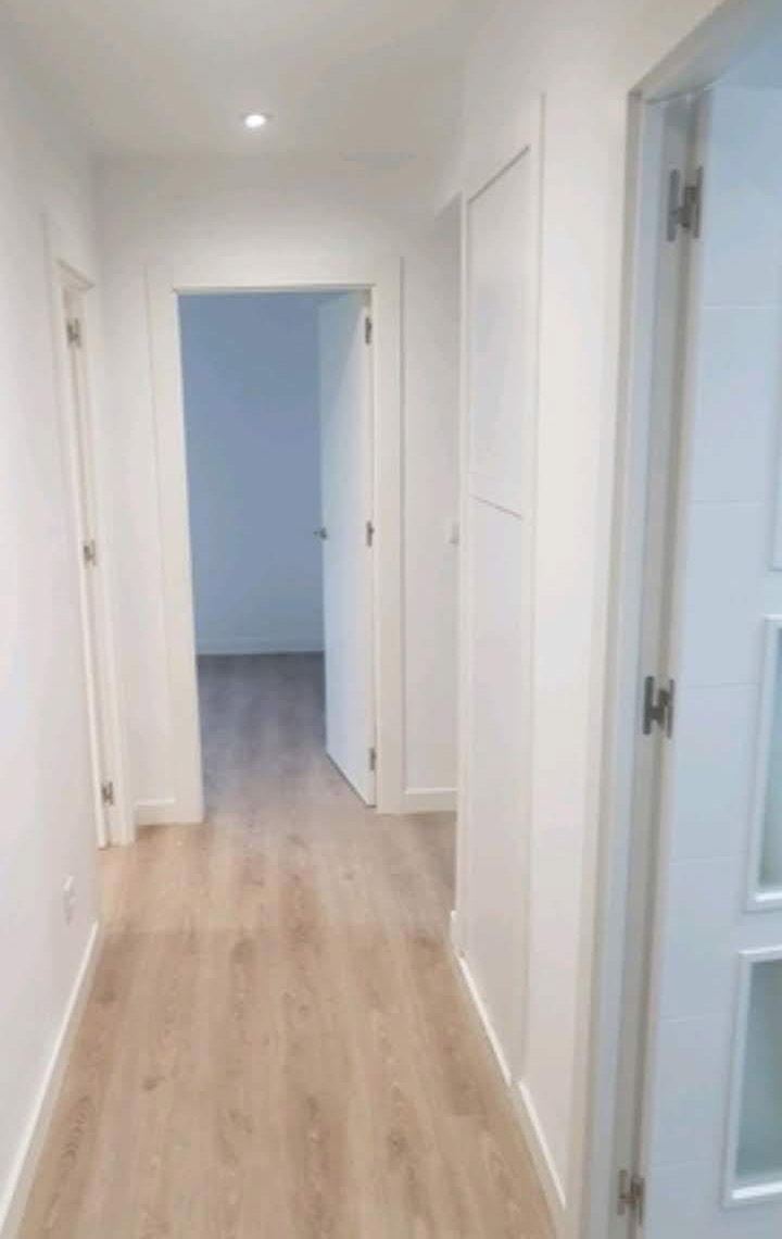 Un largo pasillo con pisos de madera y paredes blancas que conduce a un dormitorio.