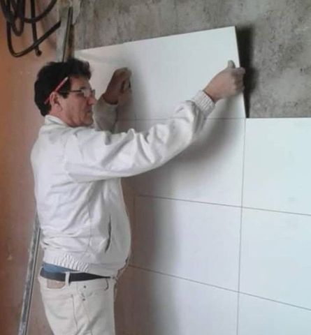 Un hombre con una chaqueta blanca está instalando azulejos blancos en una pared.