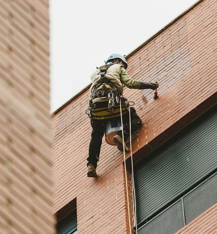 Un hombre está pintando el costado de un edificio de ladrillos.