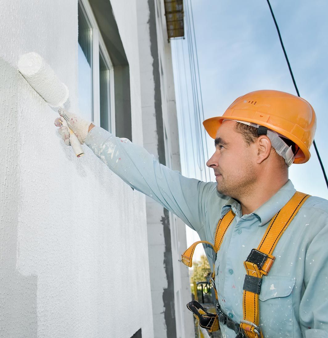 Un hombre que lleva un casco naranja está pintando una pared.