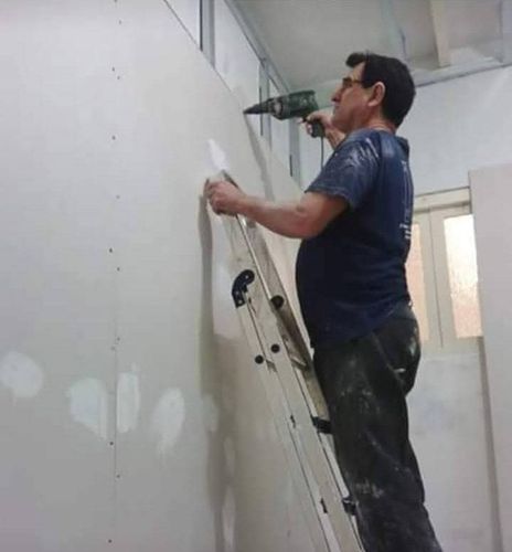 Un hombre de pie en una escalera usando un taladro en una pared.