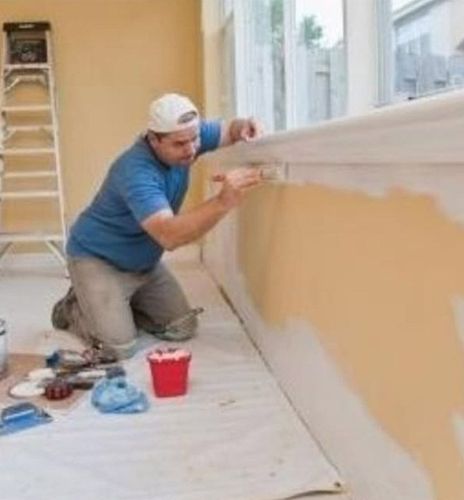 Un hombre está arrodillado y pintando una pared.