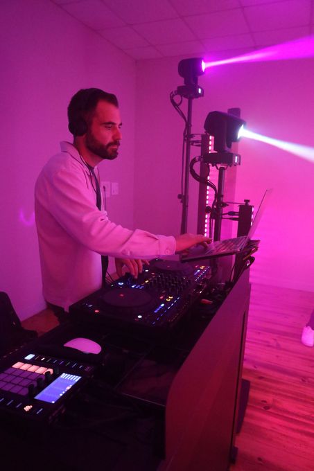 Un DJ mixe dans une salle éclairée en rose et violet, les projecteurs de scène projetant des faisceaux vers la droite.